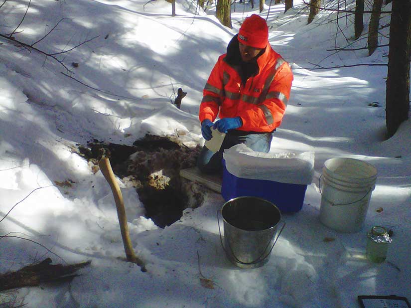 Man taking a dirt sample from a hold in the snow